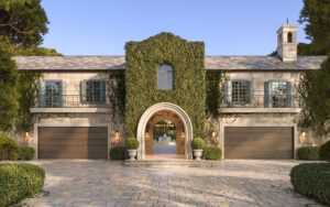 A beautiful stone house with ivy-covered walls, two garage doors, and a rounded entrance. Green shrubs line the path.