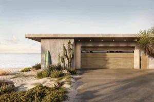 A modern beachfront house with a concrete facade, wooden garage door, a surfboard, and desert plants.