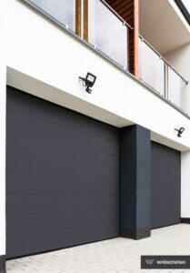 Modern dark gray garage doors with horizontal lines, a balcony above, and stylish lighting.