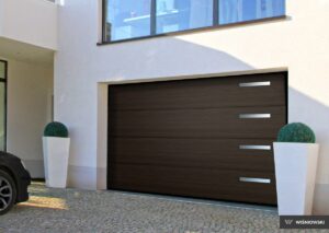 A modern garage door with horizontal wooden panels and silver handles, beside planters with bushy greenery.