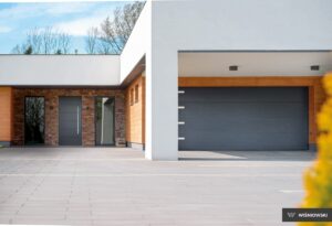 Modern home entrance with a gray door, stone wall, large window, and garage.
