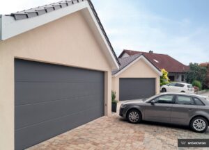 Two garages with gray doors and a gray car parked in a stone driveway.