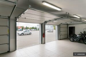 A spacious garage with two open doors, revealing a parking lot with cars outside.