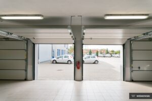 A view from inside a garage showing two open doors, two parked cars, and a tiled floor.