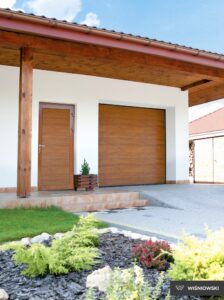 A modern house entrance featuring a brown door and garage, surrounded by plants and flowers.
