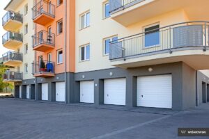 A modern apartment building with orange accents and balconies, featuring individual white garage doors.