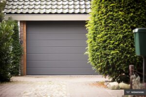 A pristine, modern full-view sectional garage door with large glass panels framed in sleek, black aluminum. The door is slightly open, showcasing its seamless operation and clean design. Ideal for enhancing the curb appeal of contemporary homes and offering abundant natural light into the garage space.